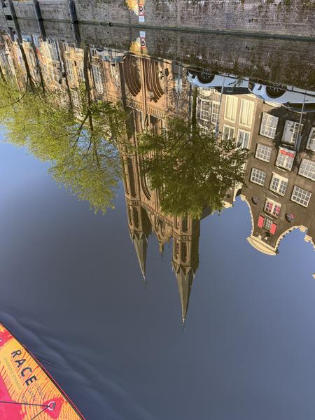 A serene view captures the reflections of historic Amsterdam canal houses and a grand church in the calm waters of the Singel canal in Centrum